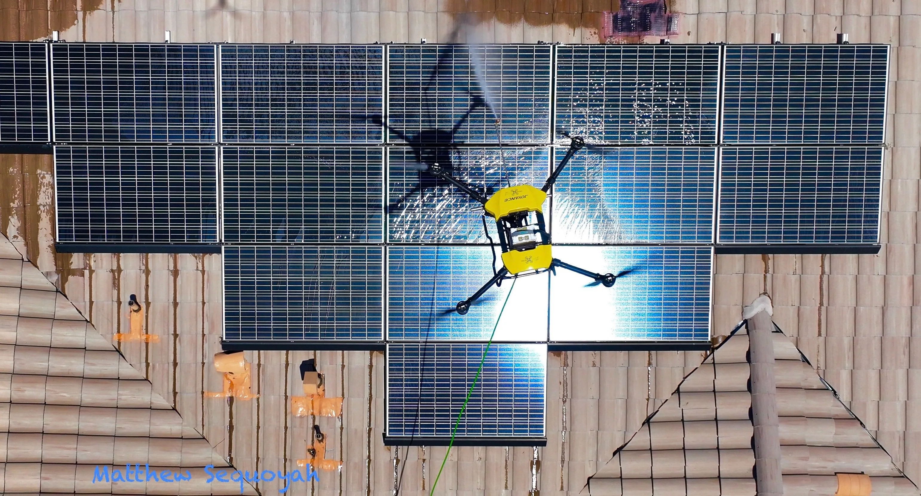 Top-down view of the drone parked over the array, water tracking across the panels