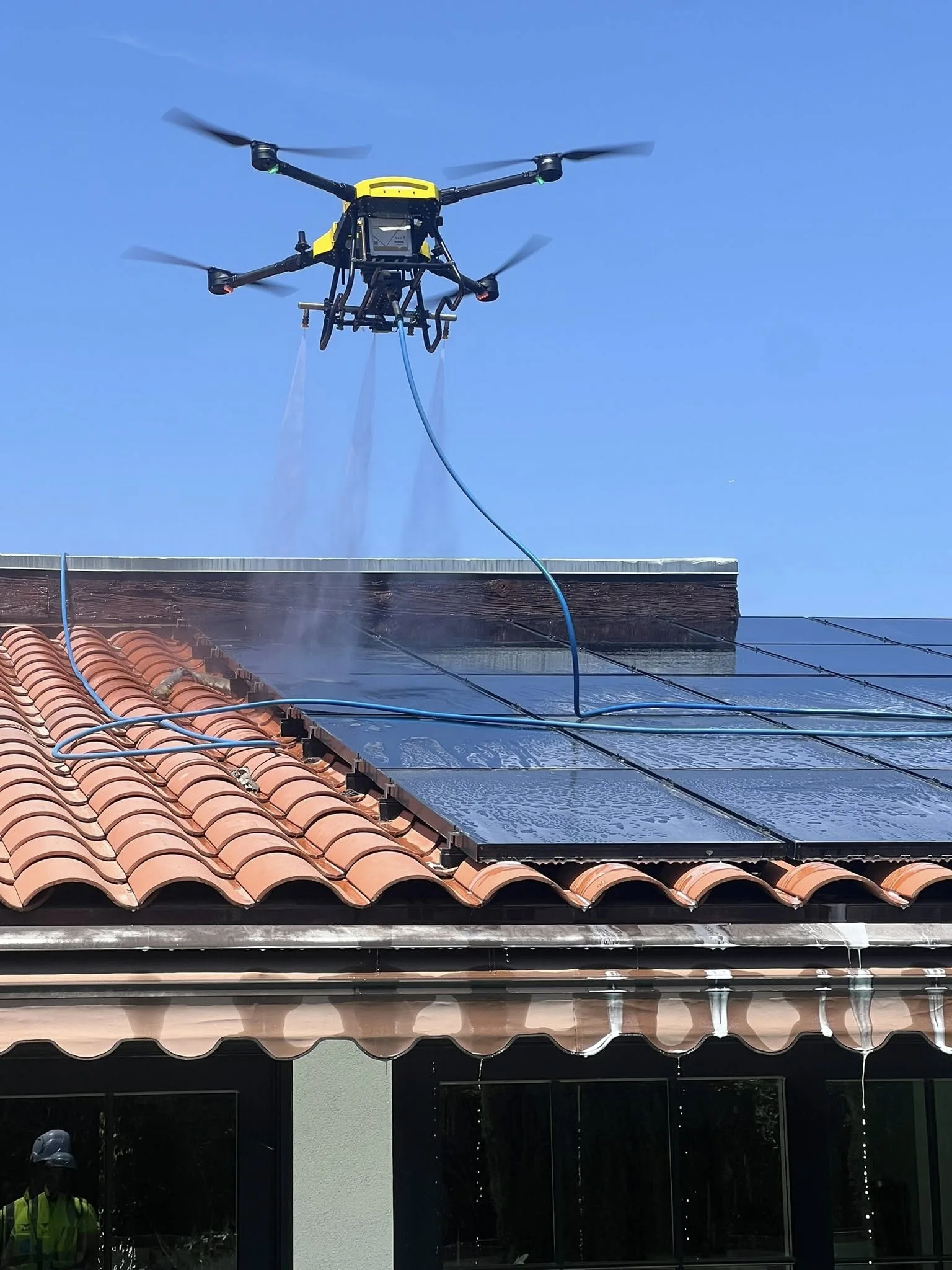 Yellow Drone Power 1 aircraft spraying deionized water onto solar panels on a tile roof