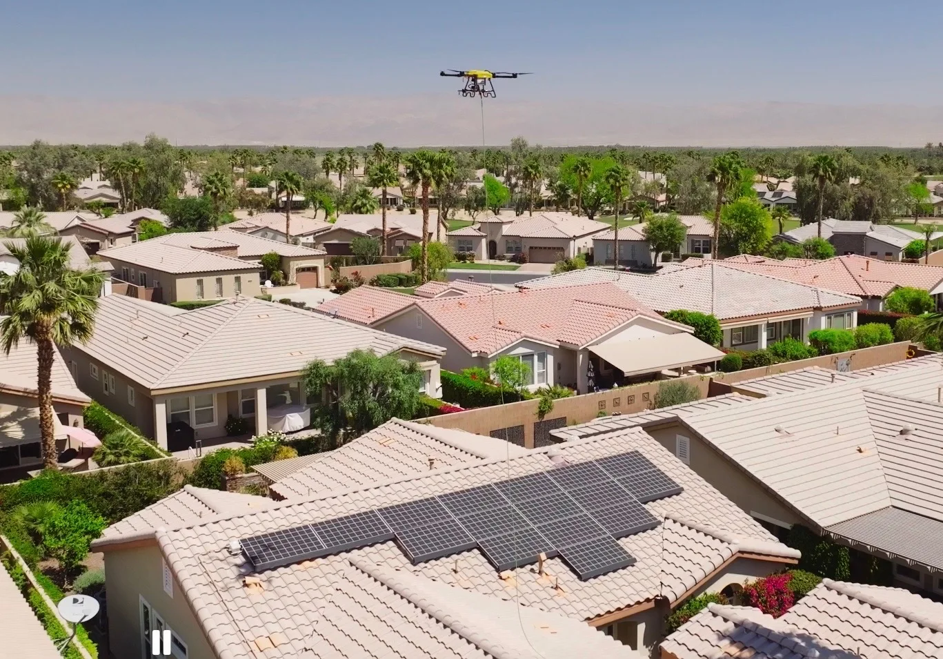 Wider neighborhood frame with the drone holding above a tile-roof array — the suburban context of every job we fly.